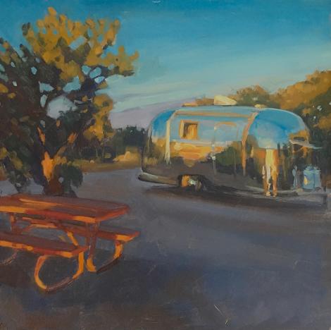 vintage airstream trailer at a campsite with picnic bench at sunrise