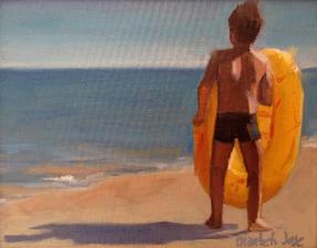 boy with yellow plastic dinghy contemplates the ocean from the beach